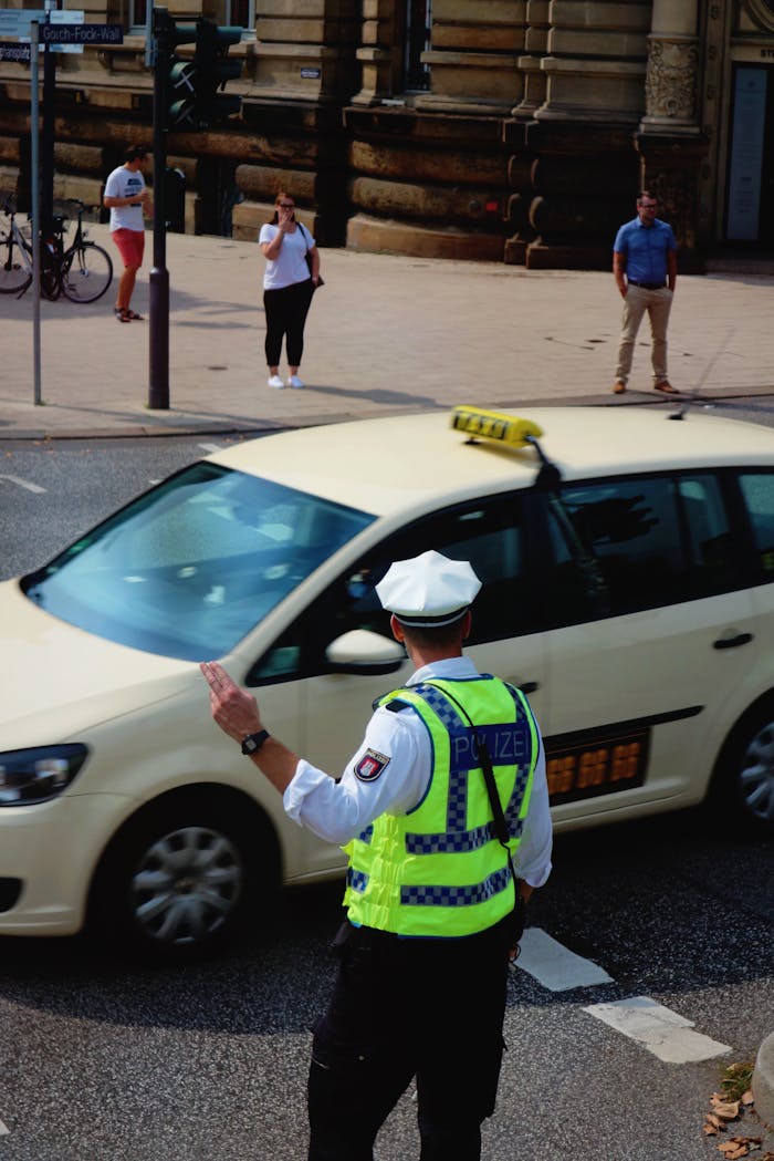 A policeman in uniform directs traffic with a taxi and pedestrians in central Hamburg.